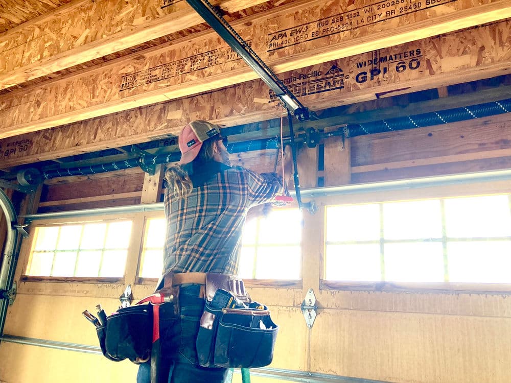 Woman repairing garage door opener with tools in a home garage setting.