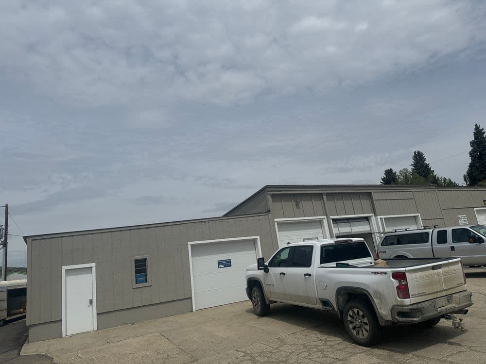 Gray industrial building with a white pickup truck in front under a cloudy sky.
