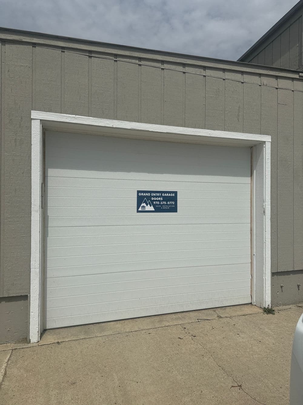 White garage door with a blue sign for Grand Entry Garage located in a residential area.