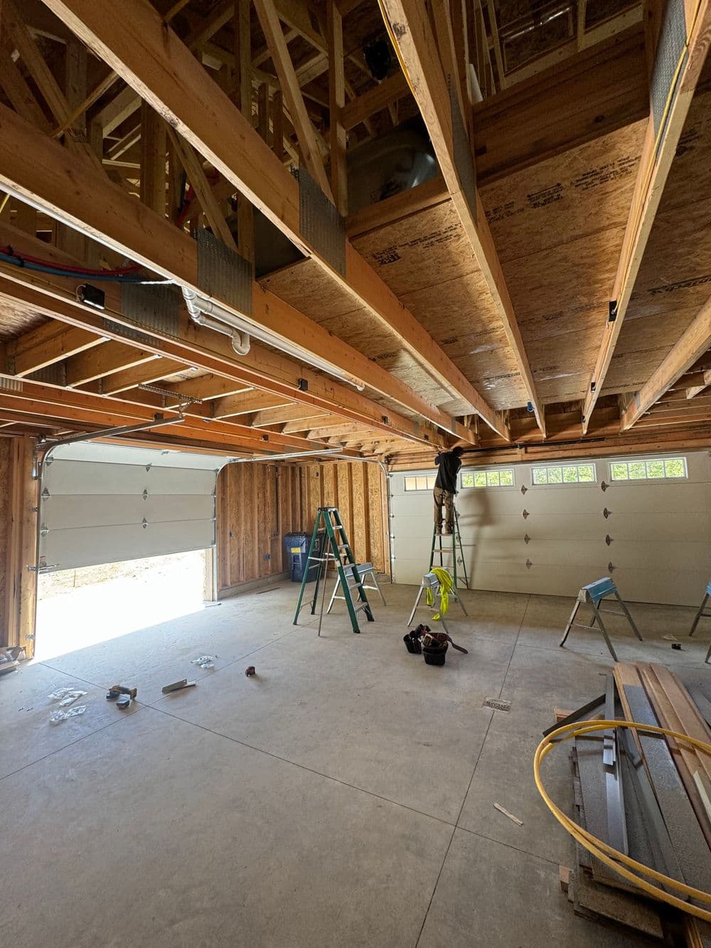 Interior of a garage under construction, featuring wooden beams, tools, and a ladder.