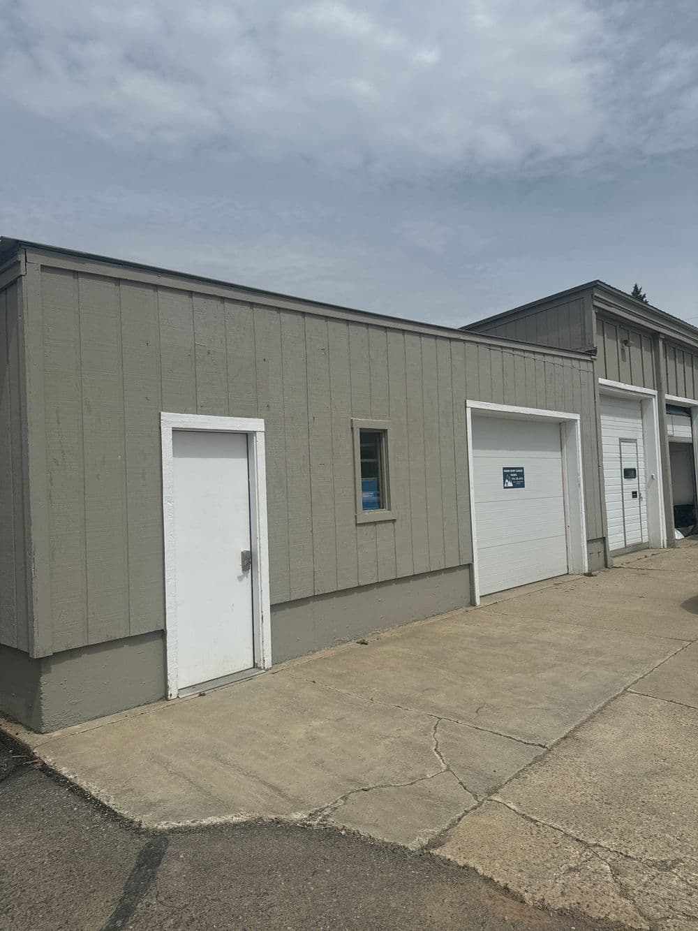 Gray commercial building with two garage doors and a side entrance on a concrete lot.
